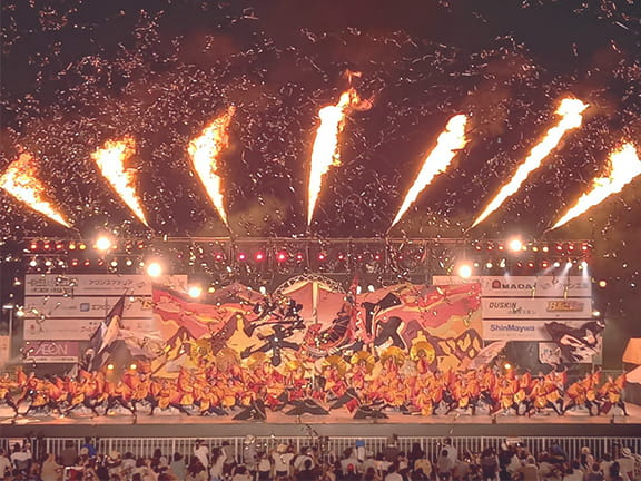 炎が立ち上るステージで、そろいの衣装で踊る演者